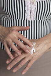 Ältere Frau trägt zu Hause Lotion auf die Hand auf - FCF01980