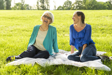 Smiling senior woman with mid-adult woman sitting on picnic blanket at public park - OIPF00875