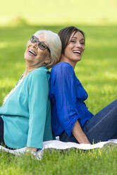 Smiling senior woman sitting with mid-adult woman in public park - OIPF00880