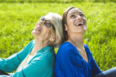 Happy senior woman and mid-adult woman looking up while sitting in public park - OIPF00881