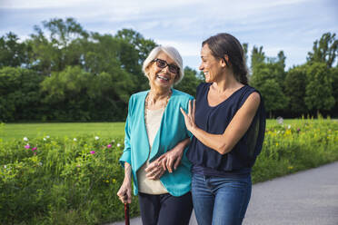 Pflegende Frau im mittleren Erwachsenenalter mit älterer Frau beim Spaziergang im Park - OIPF00900