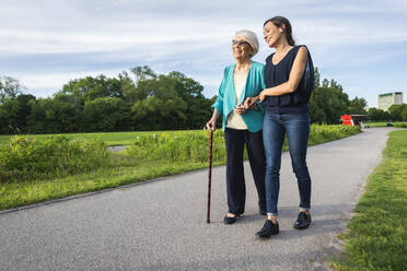 Lächelnde ältere Frau mit halbwüchsiger Frau auf dem Fußweg im Park - OIPF00901