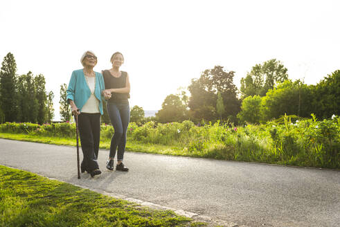 Mittlere erwachsene Frau, die eine ältere Frau beim Spazierengehen im Park stützt - OIPF00902