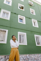 Nachdenkliche Frau vor grünem Gebäude stehend - TCEF01923