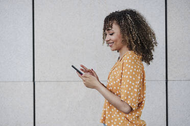 Junge Frau benutzt Smartphone an der Wand - EBBF03903