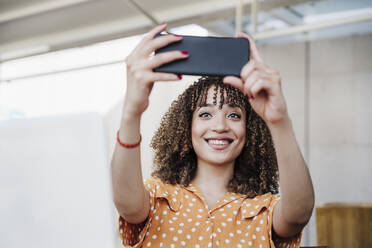 Smiling young woman taking selfie through smart phone in cafe - EBBF03934