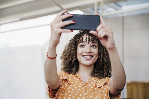 Lächelnde junge Frau nimmt Selfie durch Smartphone in Café - EBBF03934