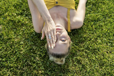 Woman covering eye while lying on grass - AFVF08862