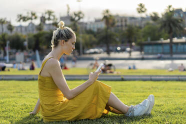 Frau, die im Gras sitzend eine SMS über ihr Mobiltelefon verschickt - AFVF08864