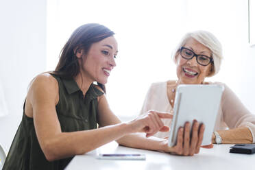 Lächelnde Frau zeigt digitales Tablet im Gespräch mit Großmutter zu Hause - OIPF00904