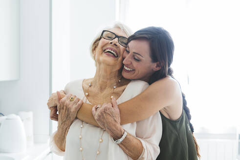 Cheerful woman hugging grandmother in kitchen at home - OIPF00910