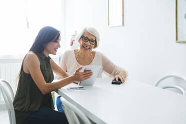 Lächelnde Großmutter und Enkelin teilen sich ein digitales Tablet, während sie am Tisch sitzen - OIPF00933