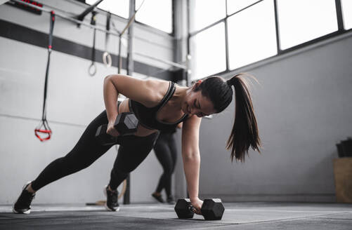 Lächelnde Frau beim Training mit Hanteln im Fitnessstudio - SNF01482