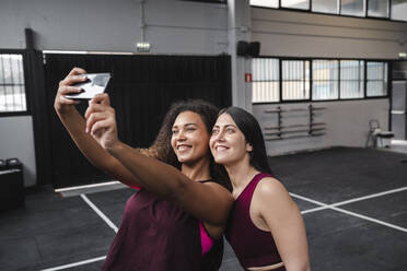 Lächelnde Sportlerinnen nehmen Selfie durch Handy im Fitnessstudio - SNF01491