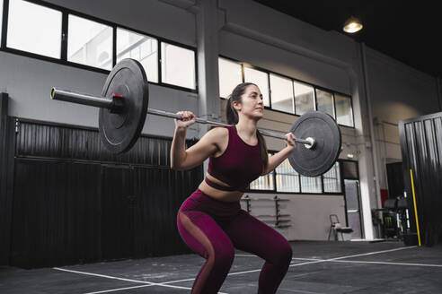 Weibliche Athletin trainiert mit Langhantel im Fitnessstudio - SNF01493