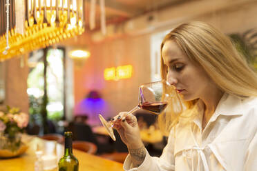 Junge blonde Frau trinkt Rotwein und sitzt an der Bar - VGF00389