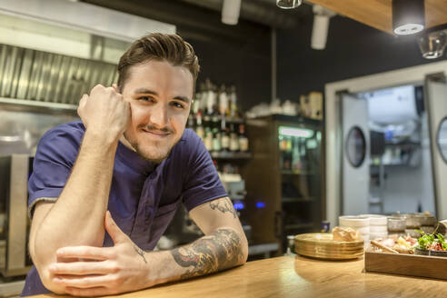 Lächelnder männlicher Barkeeper, der sich auf den Bartresen stützt - VGF00403