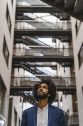 Male entrepreneur looking up while standing amidst buildings - AFVF08887