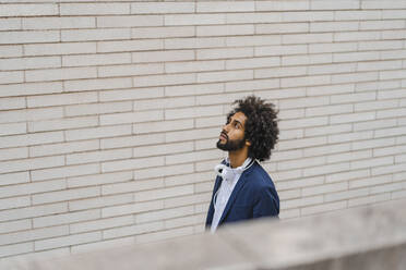 Male entrepreneur looking away while standing by brick wall - AFVF08906