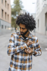 Young man looking at plaid shirt while standing on footpath - AFVF08919