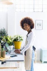 Female shop owner with laptop standing at plant store - GIOF12934