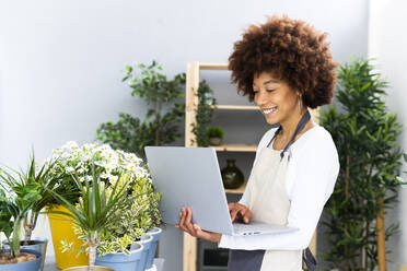 Lächelnder Florist, der einen Laptop benutzt, während er neben Pflanzen im Geschäft steht - GIOF12937