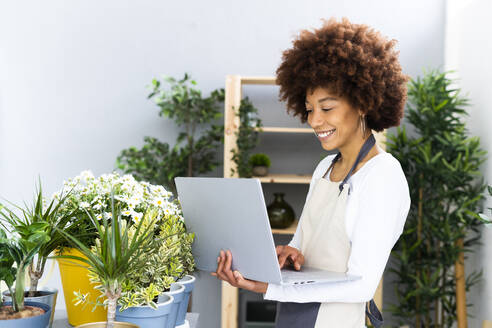 Smiling florist using laptop while standing by plants in shop - GIOF12937