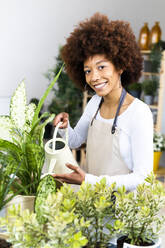 Junge Blumenhändlerin beim Gießen von Pflanzen im Geschäft - GIOF12953