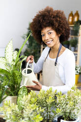 Young female florist watering plants at shop - GIOF12953