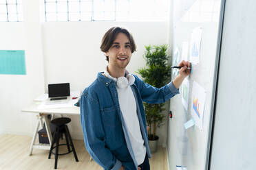 Geschäftsmann schreibt auf Haftnotiz, während er am Whiteboard im Büro steht - GIOF13003