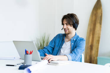 Männlicher Unternehmer mit Headset, der einen Laptop bei der Arbeit im Büro benutzt - GIOF13005
