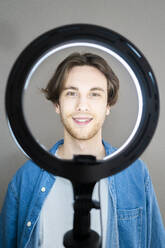 Smiling man standing in front of illuminated ring light - GIOF13015