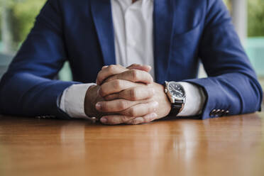 Businessman sitting with hands clasped on table - EBBF03955