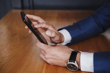 Businessman using smart phone on wooden table - EBBF03964