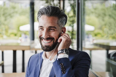 Businessman adjusting in-ear headphones at cafeteria - EBBF03971