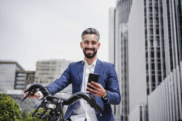 Businessman with mobile phone and rented bicycle in city - EBBF03972