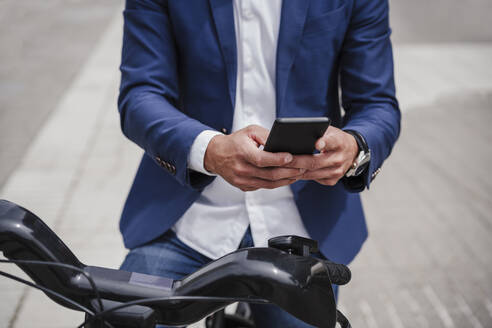 Geschäftsmann mit gemietetem Elektrofahrrad, der auf dem Gehweg ein Mobiltelefon benutzt - EBBF03974