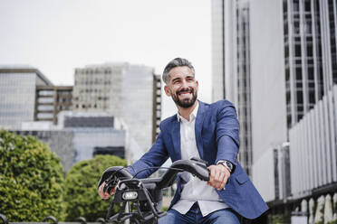 Businessman riding rented electric bicycle in city - EBBF03976