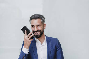 Geschäftsmann, der vor einer weißen Wand mit einem Smartphone telefoniert - EBBF03998