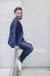 Lächelnder männlicher Unternehmer, der auf einem Geländer sitzt - EBBF04000