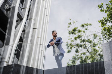 Thoughtful businessman leaning on railing during sunny day - EBBF04010