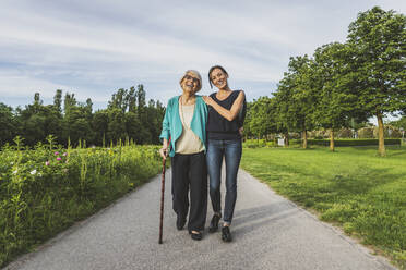 Smiling grandmother and granddaughter walking together on road at park - OIPF00951