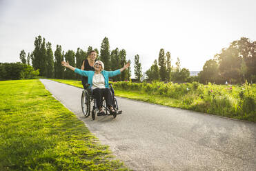 Fröhliche Enkelin spielt mit der im Rollstuhl sitzenden Großmutter im Park - OIPF00955