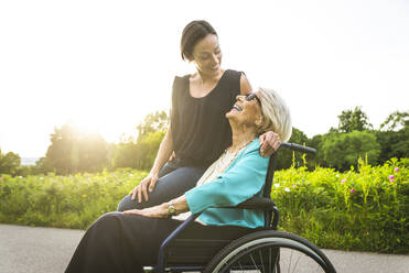 Enkelin lächelt, während sie die im Rollstuhl sitzende Großmutter betrachtet - OIPF00960