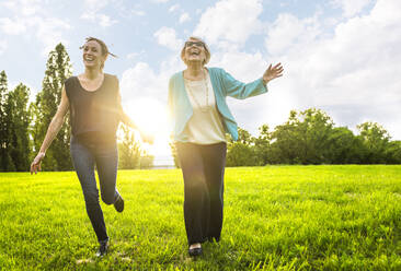 Glückliche Frauen, die sich beim Laufen auf einer Wiese an den Händen halten - OIPF00970