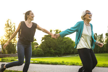 Playful grandmother holding hand of granddaughter while running in park - OIPF00973