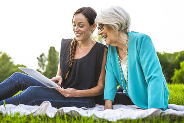 Lächelnde Frauen, die ein digitales Tablet benutzen, während sie auf einer Picknickdecke sitzen - OIPF00981