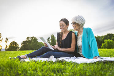 Smiling granddaughter using digital tablet while sitting by grandmother on picnic blanket - OIPF00983