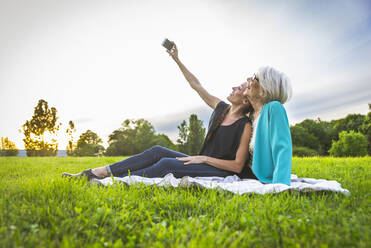 Lächelnde Frauen nehmen Selfie durch Handy beim Sitzen auf der Wiese - OIPF00984