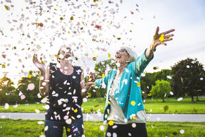 Carefree women playing with confetti while standing at park - OIPF00985